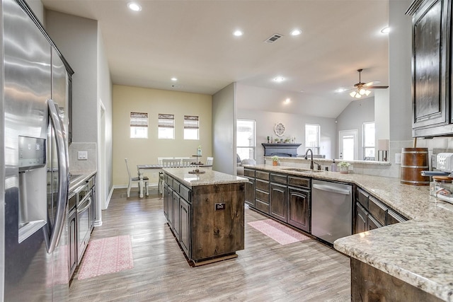 kitchen with stainless steel appliances, dark brown cabinetry, a sink, and light wood finished floors