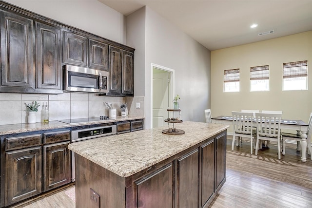 kitchen with dark brown cabinetry, stainless steel appliances, a kitchen island, light wood-style floors, and backsplash