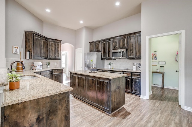 kitchen with arched walkways, a kitchen island with sink, stainless steel appliances, dark brown cabinets, and a sink