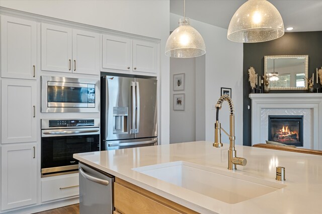 kitchen with a high end fireplace, a sink, light countertops, appliances with stainless steel finishes, and decorative light fixtures