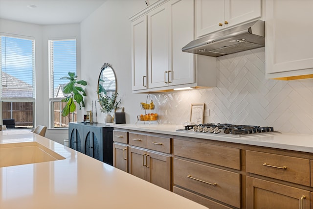 kitchen featuring under cabinet range hood, stainless steel gas cooktop, light countertops, and a wealth of natural light