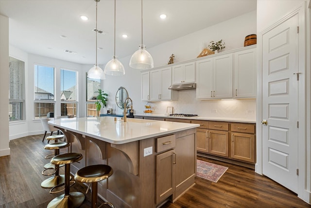 kitchen with a breakfast bar, light countertops, dark wood-style floors, and under cabinet range hood