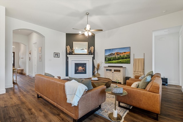 living area with baseboards, arched walkways, dark wood-type flooring, and a glass covered fireplace