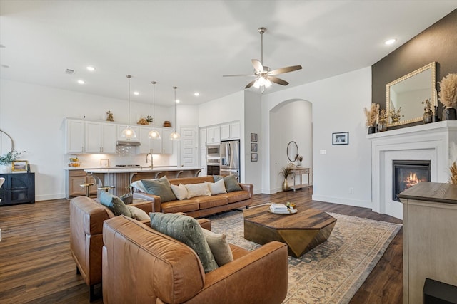 living area with dark wood-style floors, recessed lighting, arched walkways, ceiling fan, and a glass covered fireplace