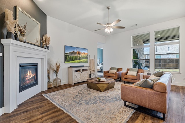 living area with dark wood finished floors, a glass covered fireplace, baseboards, and visible vents