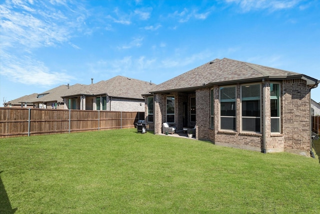 rear view of property featuring brick siding, a fenced backyard, a lawn, and a shingled roof