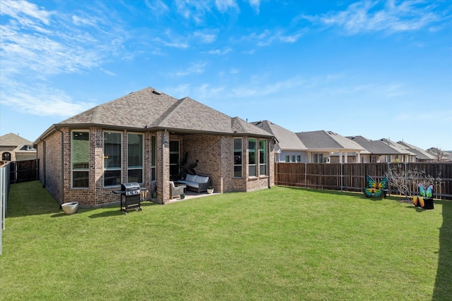 back of property with brick siding, roof with shingles, a yard, a fenced backyard, and a patio