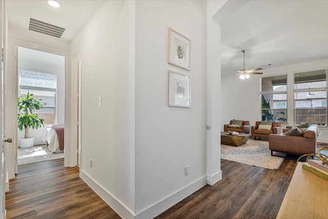 hallway with dark wood-style floors, visible vents, arched walkways, and baseboards