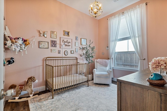 bedroom featuring wood finished floors, visible vents, baseboards, an inviting chandelier, and a crib