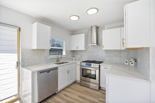 kitchen featuring a sink, white cabinetry, wall chimney range hood, appliances with stainless steel finishes, and light wood-type flooring