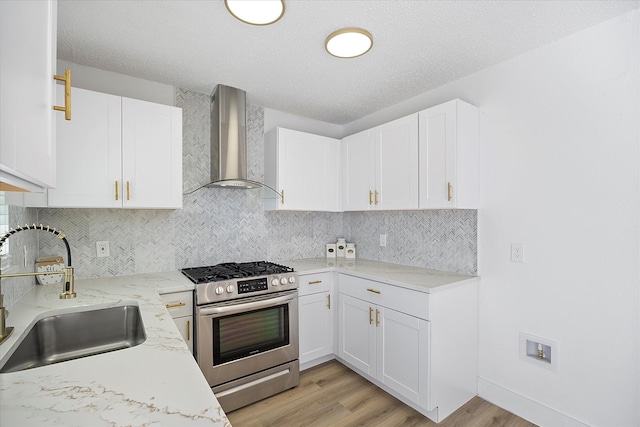 kitchen featuring tasteful backsplash, white cabinets, wall chimney exhaust hood, stainless steel range with gas stovetop, and a sink