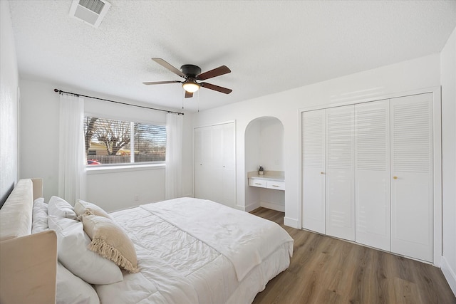 bedroom featuring a textured ceiling, wood finished floors, visible vents, a ceiling fan, and two closets