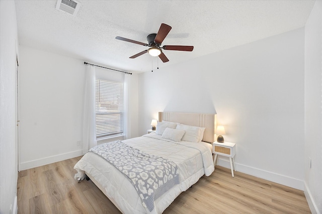 bedroom featuring light wood finished floors, visible vents, a ceiling fan, a textured ceiling, and baseboards