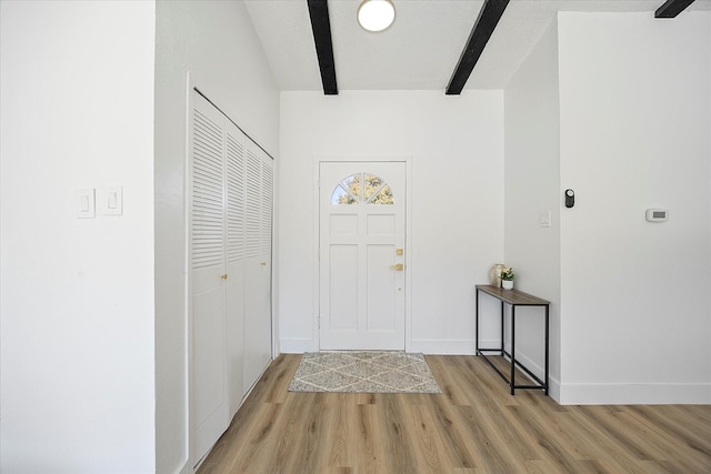 entryway featuring light wood-style flooring, baseboards, and beam ceiling