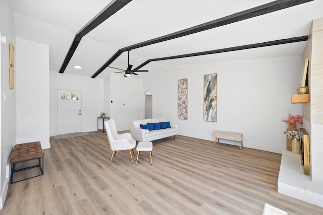 sitting room with arched walkways, vaulted ceiling with beams, a ceiling fan, light wood-style floors, and baseboards