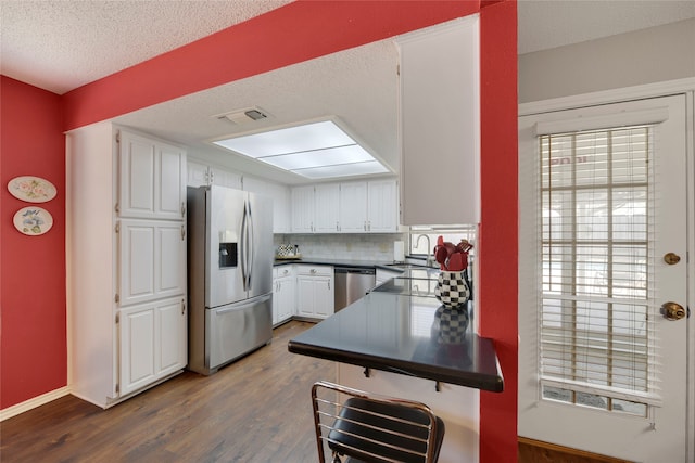 kitchen with visible vents, a sink, dark countertops, stainless steel appliances, and white cabinets