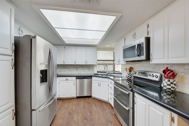 kitchen featuring dark wood finished floors, a sink, stainless steel appliances, white cabinetry, and dark countertops