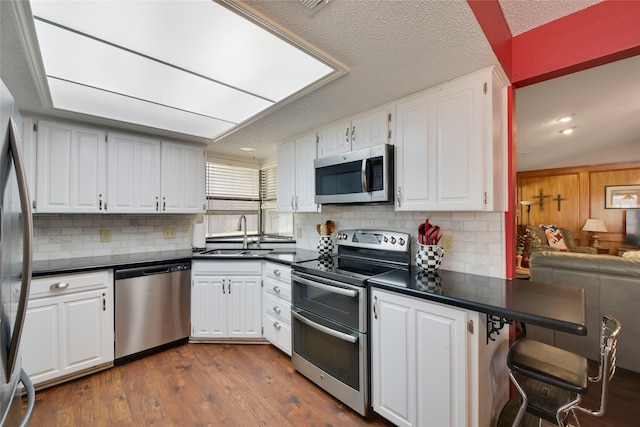 kitchen featuring dark countertops, dark wood-style floors, white cabinets, stainless steel appliances, and a sink