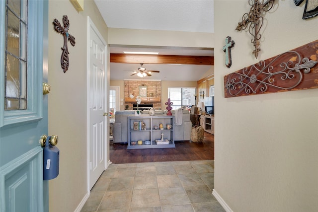 foyer entrance featuring vaulted ceiling with beams, baseboards, a fireplace, a textured ceiling, and a ceiling fan