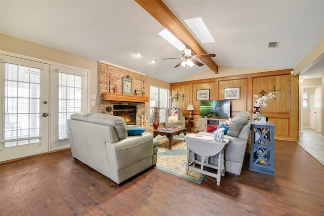 living room with wood finished floors, visible vents, a ceiling fan, vaulted ceiling with skylight, and a brick fireplace