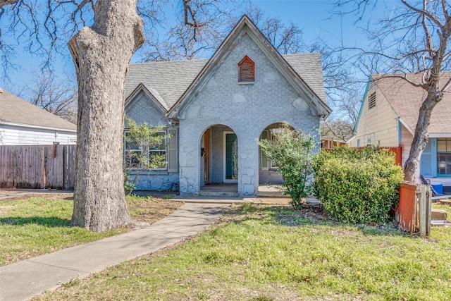 view of front of home featuring a shingled roof, a front yard, fence, and brick siding