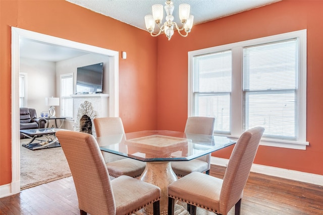 dining room featuring a textured ceiling, a fireplace, baseboards, wood-type flooring, and an inviting chandelier