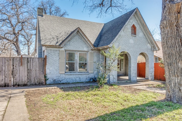 view of front of property with roof with shingles, brick siding, a chimney, a front yard, and fence