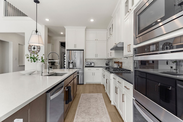 kitchen featuring glass insert cabinets, stainless steel appliances, under cabinet range hood, pendant lighting, and a sink