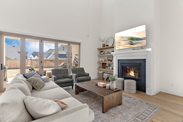 living room featuring a towering ceiling, light wood finished floors, baseboards, and a glass covered fireplace