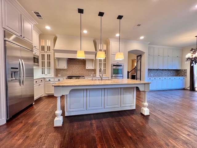 kitchen featuring built in appliances, arched walkways, a sink, visible vents, and white cabinets