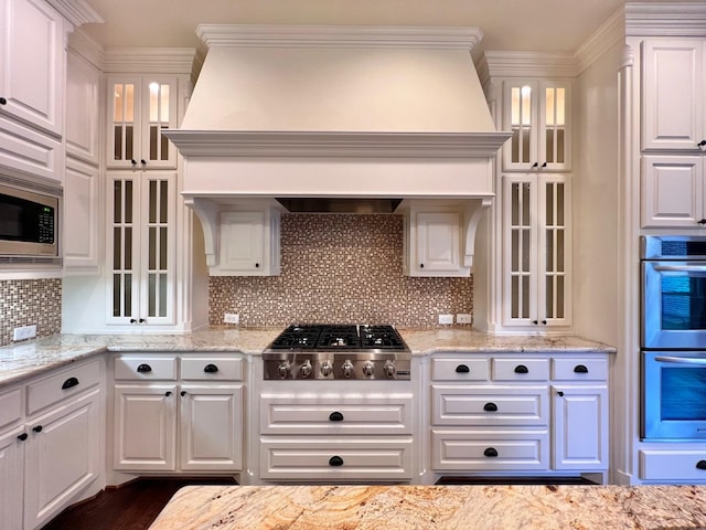 kitchen with white cabinets, decorative backsplash, custom range hood, ornamental molding, and stainless steel appliances