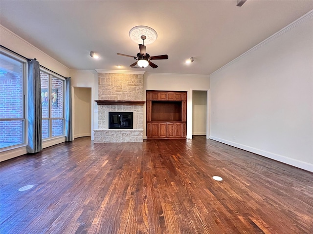 unfurnished living room featuring baseboards, dark wood finished floors, ceiling fan, crown molding, and a stone fireplace