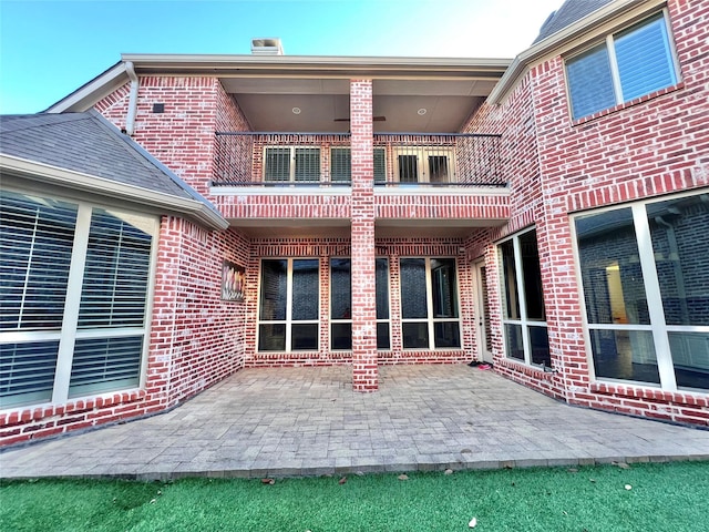 back of property featuring a patio, brick siding, and a balcony