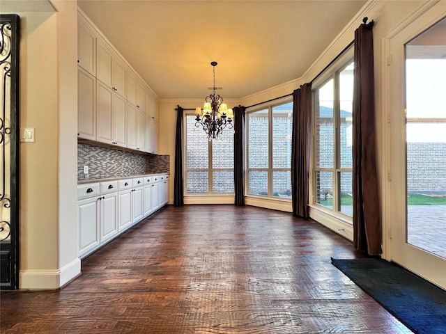 unfurnished dining area with an inviting chandelier, ornamental molding, and dark wood finished floors