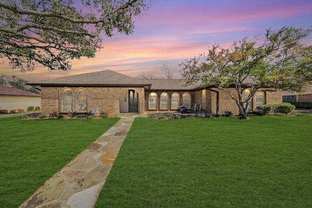 view of front facade with a shingled roof, brick siding, and a lawn