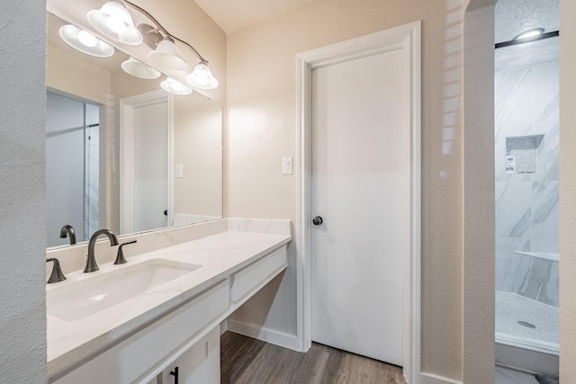 bathroom with a walk in shower, vanity, baseboards, and wood finished floors