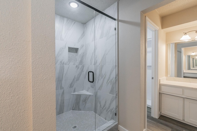 bathroom with a stall shower, a textured wall, vanity, and wood finished floors