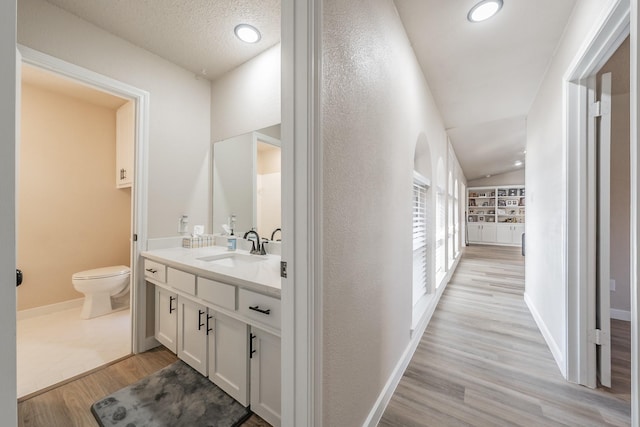 hallway featuring a textured ceiling, lofted ceiling, light wood-style flooring, a sink, and baseboards