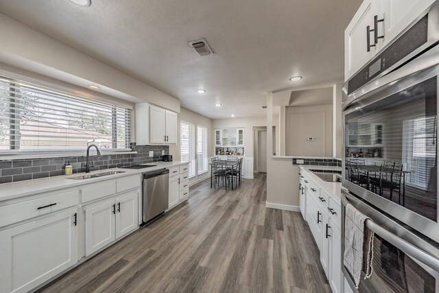 kitchen featuring tasteful backsplash, wood finished floors, stainless steel appliances, white cabinetry, and a sink