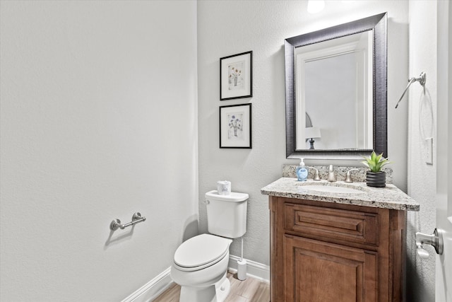 half bath with wood finished floors, vanity, toilet, and baseboards