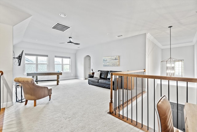 carpeted living room with baseboards, visible vents, arched walkways, crown molding, and ceiling fan with notable chandelier