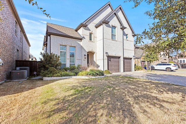 view of front of home with an attached garage, central air condition unit, concrete driveway, stucco siding, and a front yard