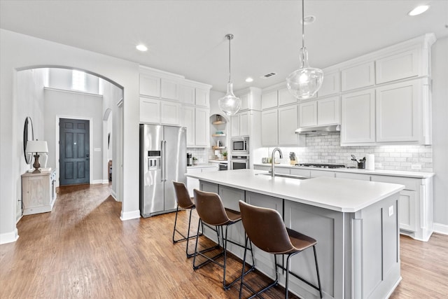 kitchen featuring an island with sink, under cabinet range hood, appliances with stainless steel finishes, and light countertops