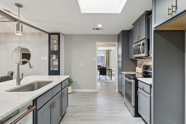 kitchen featuring hanging light fixtures, decorative backsplash, appliances with stainless steel finishes, a sink, and light stone countertops