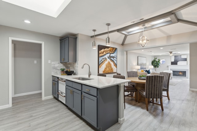 kitchen with a peninsula, a sink, tasteful backsplash, lofted ceiling with skylight, and a glass covered fireplace