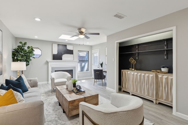 living area featuring visible vents, baseboards, light wood-style flooring, a fireplace, and recessed lighting