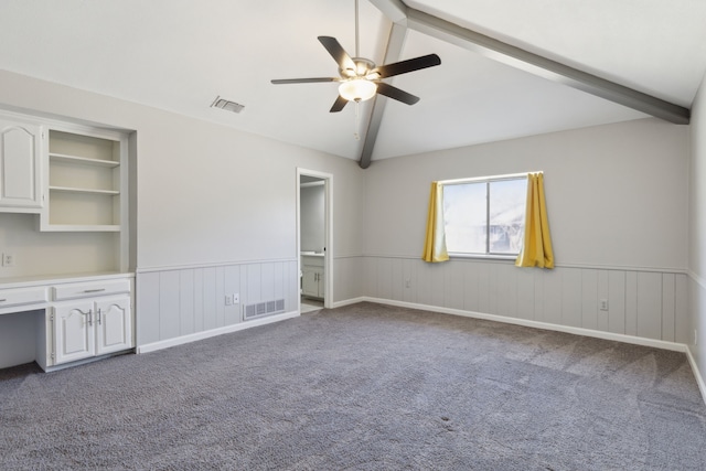 carpeted empty room featuring a wainscoted wall, visible vents, and vaulted ceiling with beams