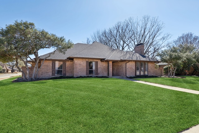 view of front of property with a shingled roof, a chimney, a front yard, and brick siding