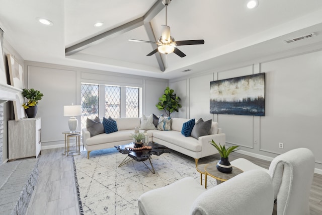 living area with a tray ceiling, visible vents, a decorative wall, and wood finished floors