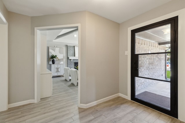 foyer featuring light wood-type flooring, a brick fireplace, and baseboards